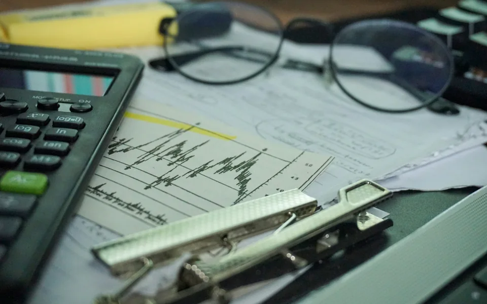 Financial paperwork, a calculator and office supplies on a desk.